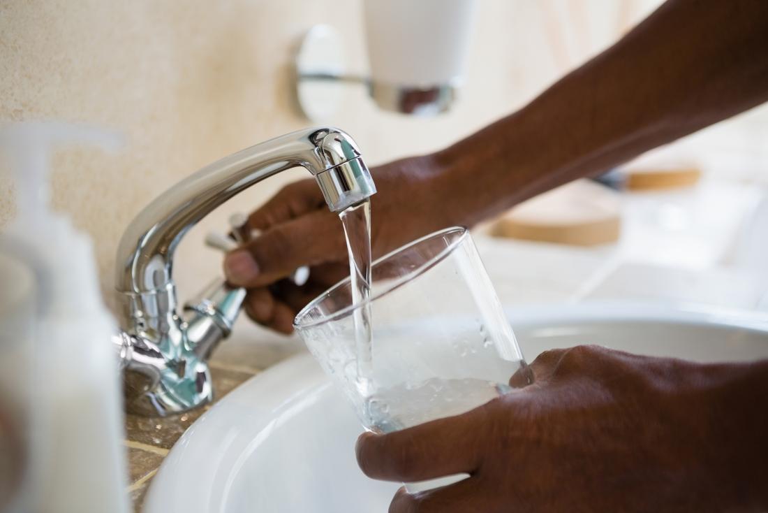 person turning on tap to pour water in glass