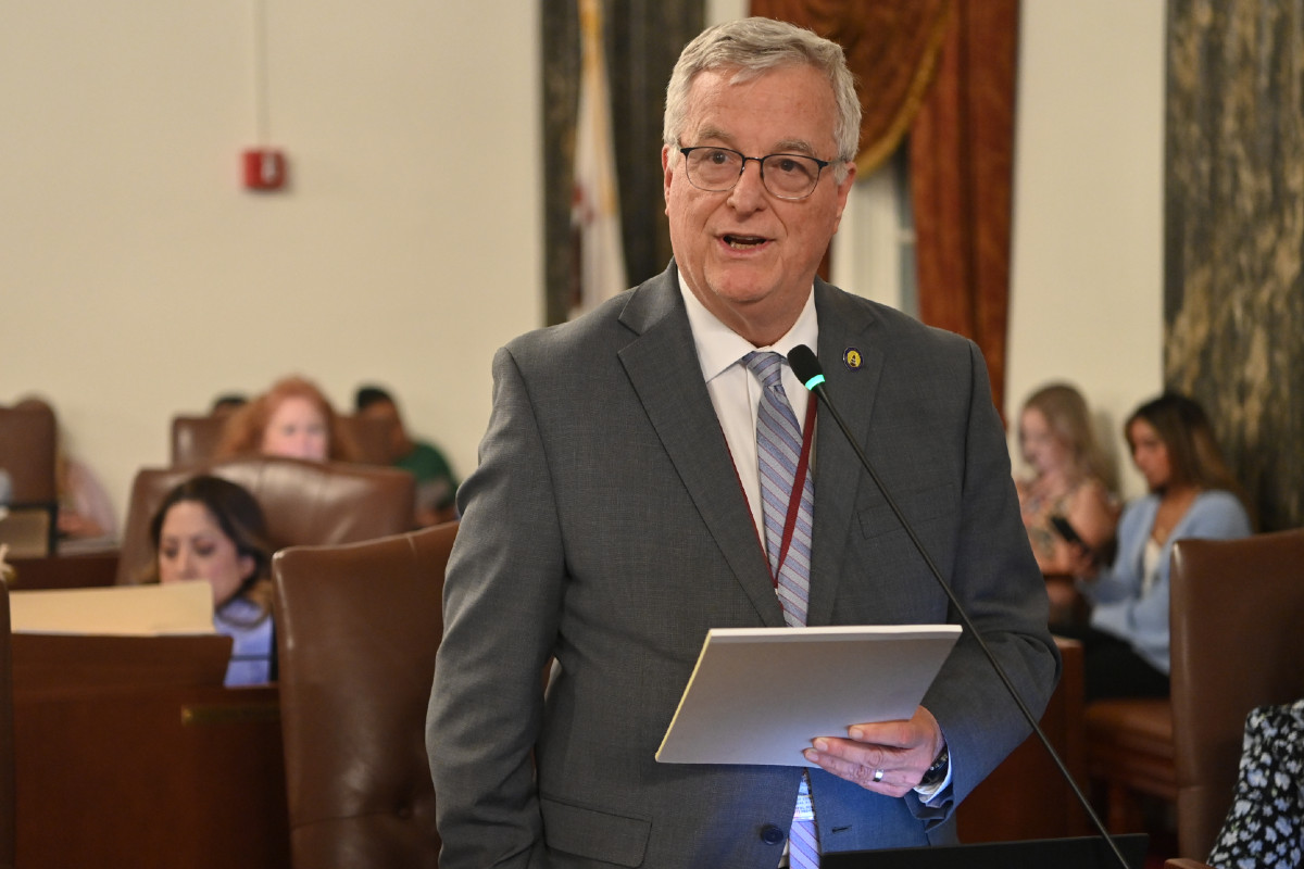 Senator Walker holds a notepad and speaks into a microphone while on the Senate floor.